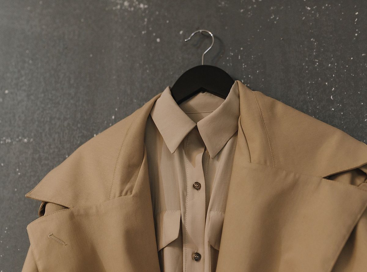 Licensed stock photograph: a tan coat over a shirt on a black hanger against a dark speckled wall.